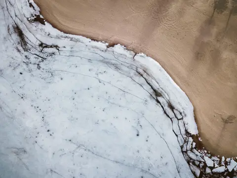 Aerial view of snow meeting sand at a shoreline